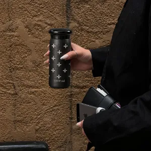 Mini tazza termica in titanio nero opaco con stelle argentate, mostrata mentre è tenuta in mano