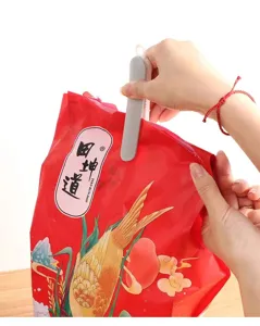 Una mano chiude il bordo di un sacchetto rosso decorato con una clip grigia in plastica