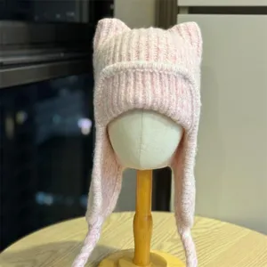 Close-up of a pale pink rib-knit hat with pointed cat ears, long earflaps, and braided ties