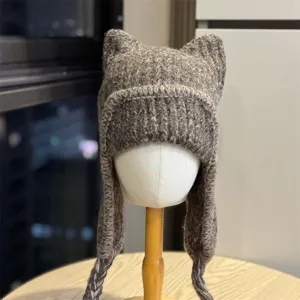 Chunky ribbed knit texture and braided earflap ties on a gray-brown hat shown on a white mannequin.