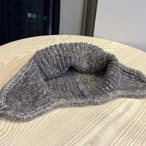 Detail of heather gray chunky knit fabric and finished edge, loosely folded on a wooden table