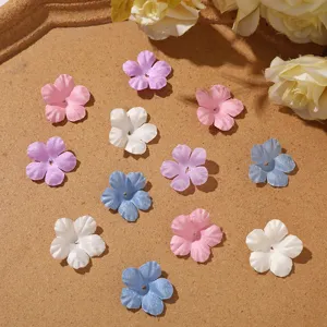 Overhead view of small five-petal fabric flowers in pink, purple, white and blue on a tan surface