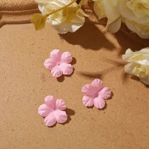 Close-up of three small pink five-petal fabric flowers arranged on a warm brown surface