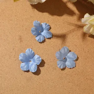 Close-up of three blue five-petal fabric flowers with center holes on a textured surface