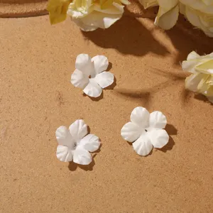 Three white five-petal fabric flowers on textured brown surface, with yellow blooms nearby