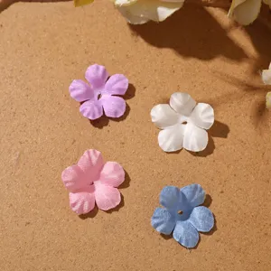 Four five-petal fabric flowers in purple, white, pink and blue, laid flat on brown paper