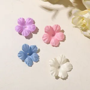 Four sheer five-petal fabric flowers in purple, pink, blue, and white on a light surface