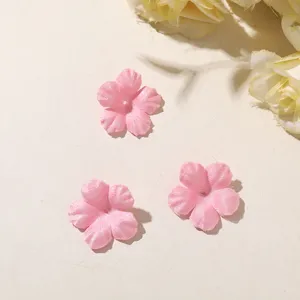 Three small pink fabric flowers with five petals and center holes, laid out on a pale beige surface.