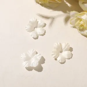 Three white five-petal fabric flowers with center holes arranged flat on a light background