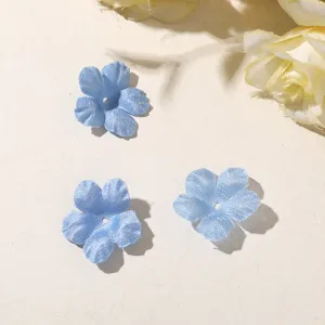 Three blue, sheer fabric flowers with perforated centers arranged on a pale tabletop