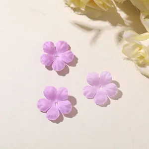 Three translucent purple five-petal fabric flowers arranged on a light beige surface