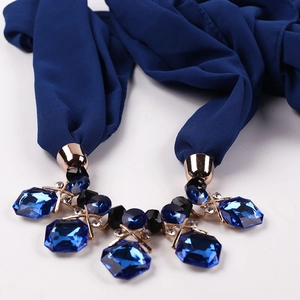 Close-up of navy chiffon scarf necklace with faceted crystal pendant and gold metal accents