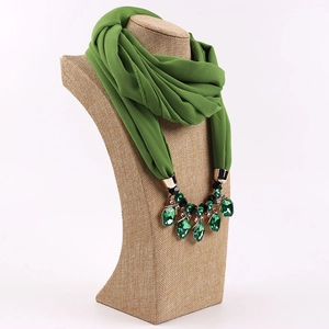 Dettaglio di sciarpa in chiffon verde scuro con collana di pietre su manichino beige