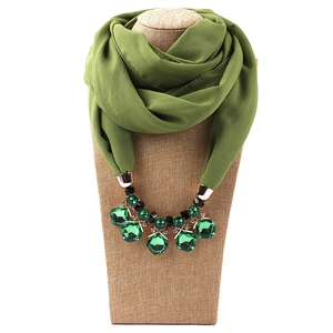 Close-up of olive green chiffon scarf necklace with gold charms and emerald-like stones