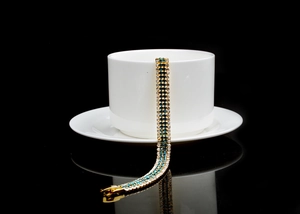 Detail shot of a layered gold-plated bracelet with blue and white crystals on a white cup