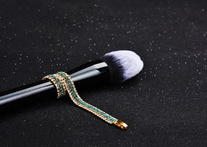 Detailed shot of a gold-plated bracelet with blue and white zircons on a makeup brush