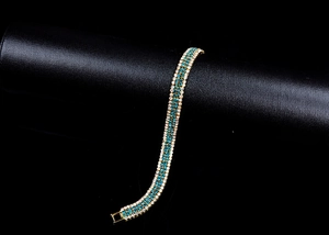 Close-up of gold-plated bracelet with blue gemstones and white diamonds on black pedestal