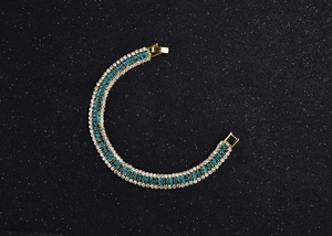 Macro detail of gold-plated bracelet with blue and clear rhinestones on black background