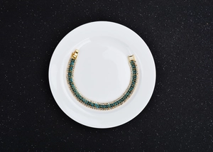 Detailed top view of a gold plated bracelet with blue and white crystals on a white plate