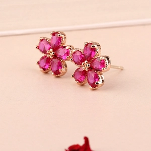 Close-up of flower-shaped stud earrings with ruby red stones and rose gold finish