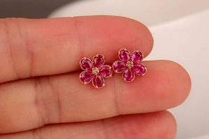 Close-up of ruby flower stud earrings in rose gold finish held on a fingertip