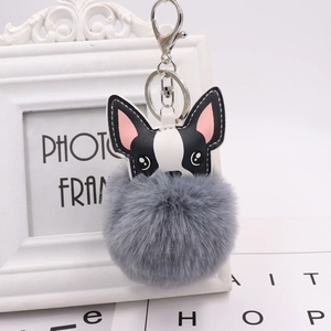 Close-up of a grey pom-pom puppy keychain with black and white leather French bulldog head
