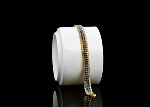 Detail of gold plated bracelet featuring rows of clear and blue sparkling crystals