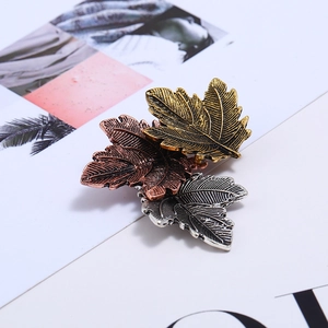 Detailed close-up of triple leaf metal brooch in antique gold, silver, and copper finishes