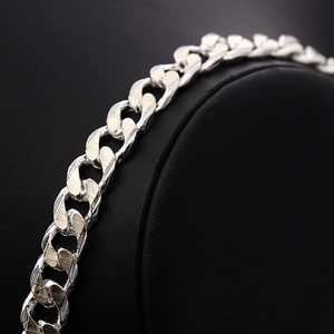 Détail macro du bracelet à maillons cubains bicolores argent et or sur présentoir noir