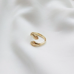 Macro shot of gold-plated hug ring featuring two hands design on white silk fabric