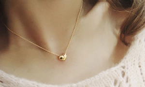 Detail of a minimalist gold heart pendant necklace worn on a woman's collarbone