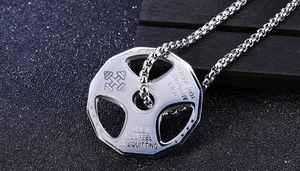 Macro detail of silver barbell weight pendant with motivational gym quote on black background