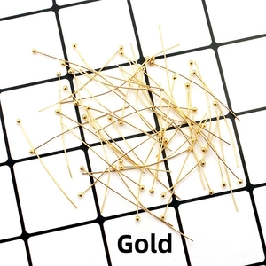 Close-up of golden ball head pins and DIY jewelry making supplies on a grid background