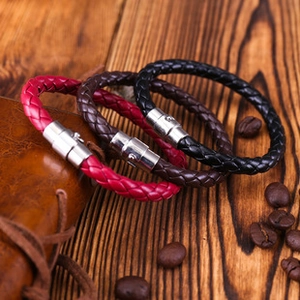 Braided leather bracelets in black, brown, and red with magnetic metal clasps on wood