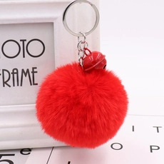 Close-up of red plush pompom keychain with a small metal bell and golden ring