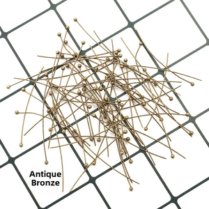 Top-down view of bronze round head pins for DIY jewelry making on grid background