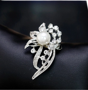 Macro shot of a floral silver brooch with a central white pearl and sparkling crystals
