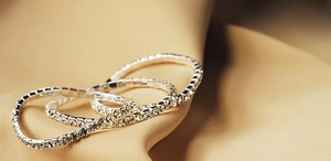 Close-up of three shimmering silver crystal elastic bracelets on a soft satin background