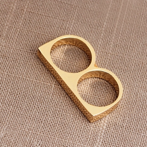 Polished gold double-finger ring featuring a B-shaped letter design on a woven surface