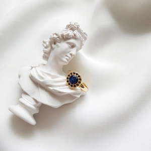 Macro view of gold sapphire ring with dark halo on a white marble sculpture