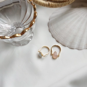 Detail of two gold rings with teardrop gemstones set against a summer shell background