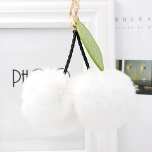 Detail of white faux fur cherry keychain with green leaf and golden metal clasp ring