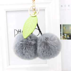 Detailed view of gray faux fur cherry keychain with green leaf and gold metal ring