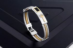 Detail of silver and gold twisted steel cable bracelet with a cross motif on metal plate