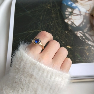 Close-up of a gold S925 silver ring with blue sapphire worn by a model in a cozy setting