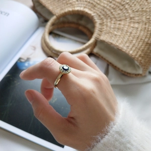 Close-up of a blue sapphire ring with a halo of diamonds on a gold-plated band worn by a model