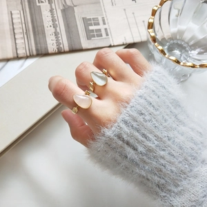 Detailed view of teardrop cat-eye stone rings in cream and pink on an adjustable gold band