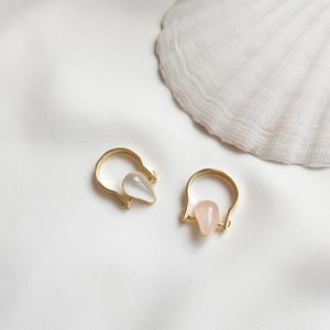 Detail of tear-shaped gold earrings with white and pink stones on white fabric