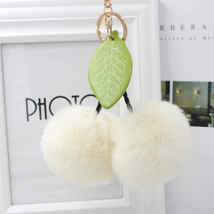 Detail view of plush cherry keychain with soft cream faux fur balls and green leaf charm