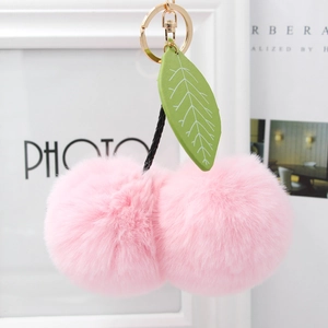Detail of pink faux fur cherry pom-poms keychain with green leather leaf and gold hardware